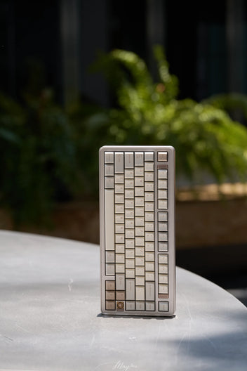 Small rectangular metal object with a geometric pattern on a reflective surface with plants in the background